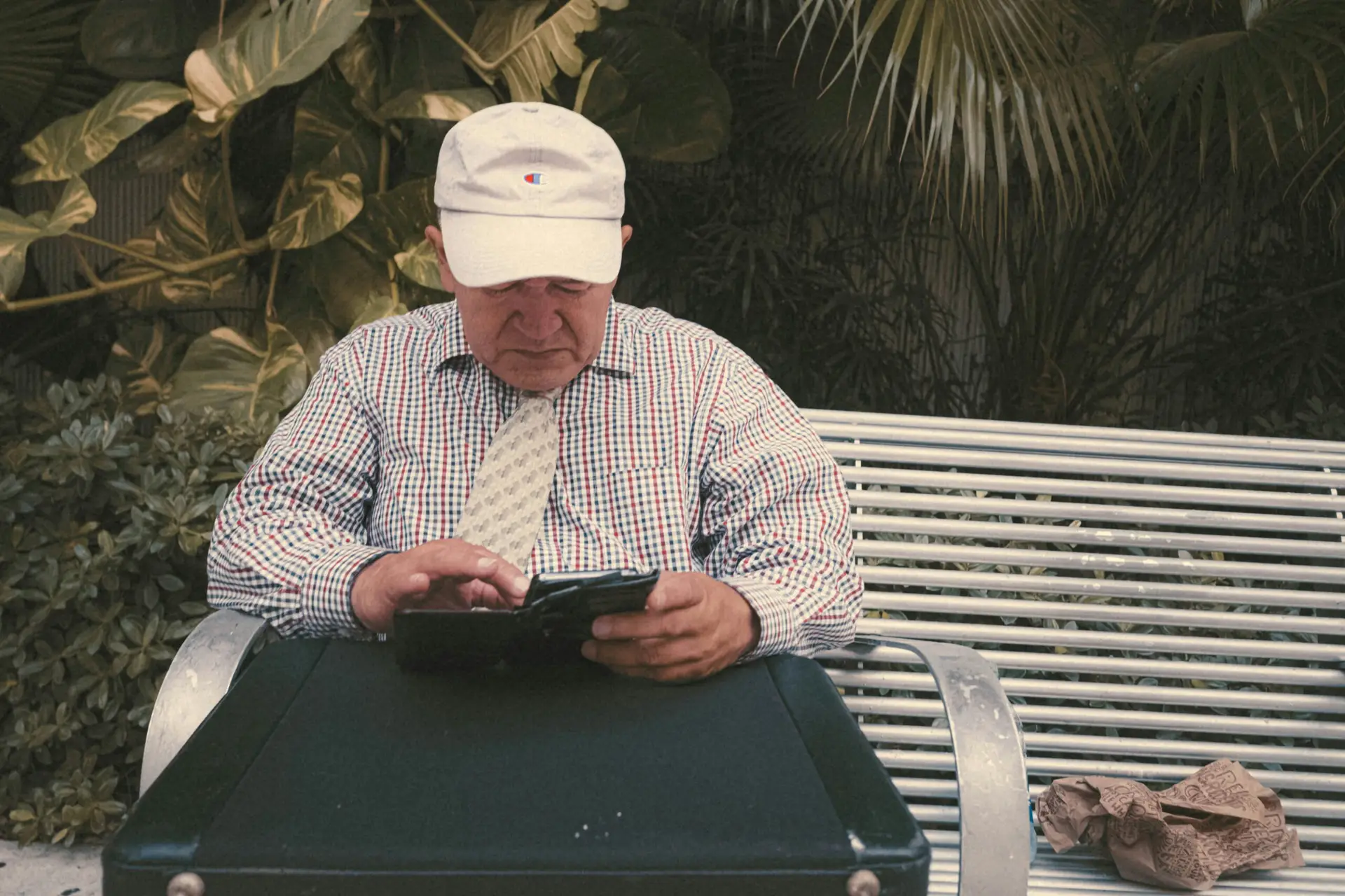Un homme âgé assi sur un banc essaie de faire que faire quelque chose sur son portable.