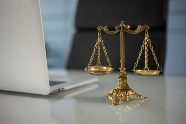 Balance dorée de la justice posée sur un bureau en verre, à côté d’un ordinateur portable.